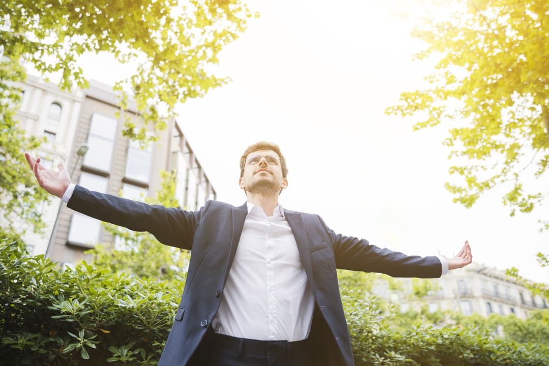 A man in suit and tie standing outside with his arms outstretched.