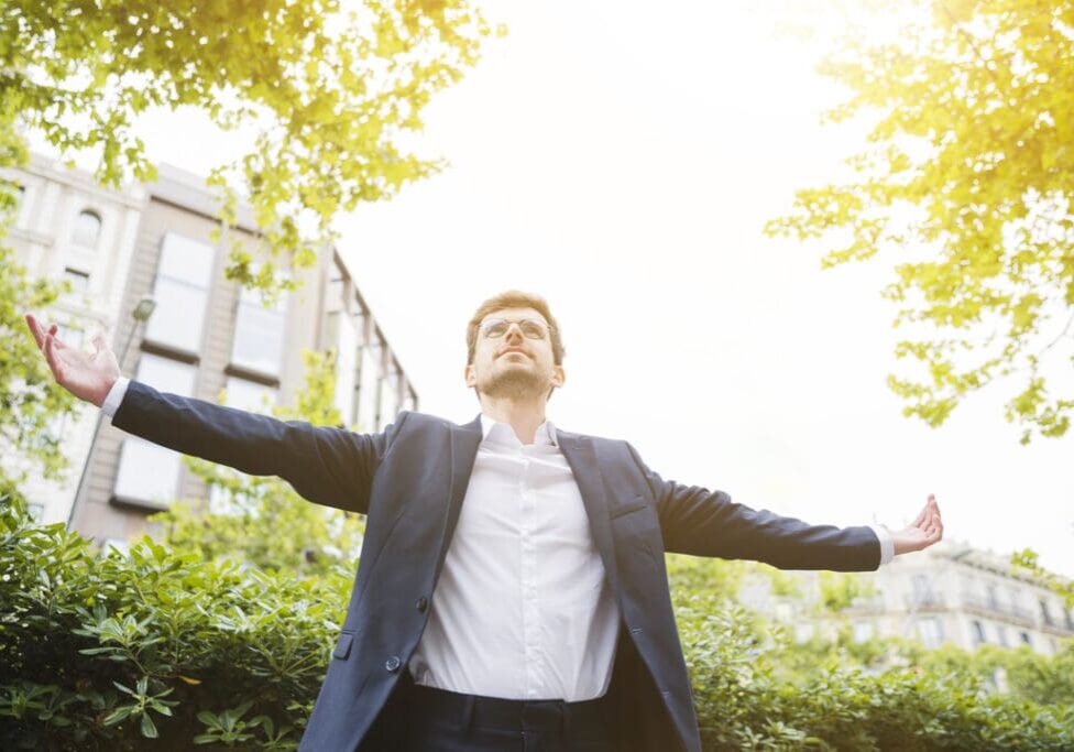 A man in suit and tie standing outside with his arms outstretched.